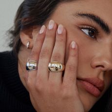 Woman wearing gold and silver rings while holding face in her hand.